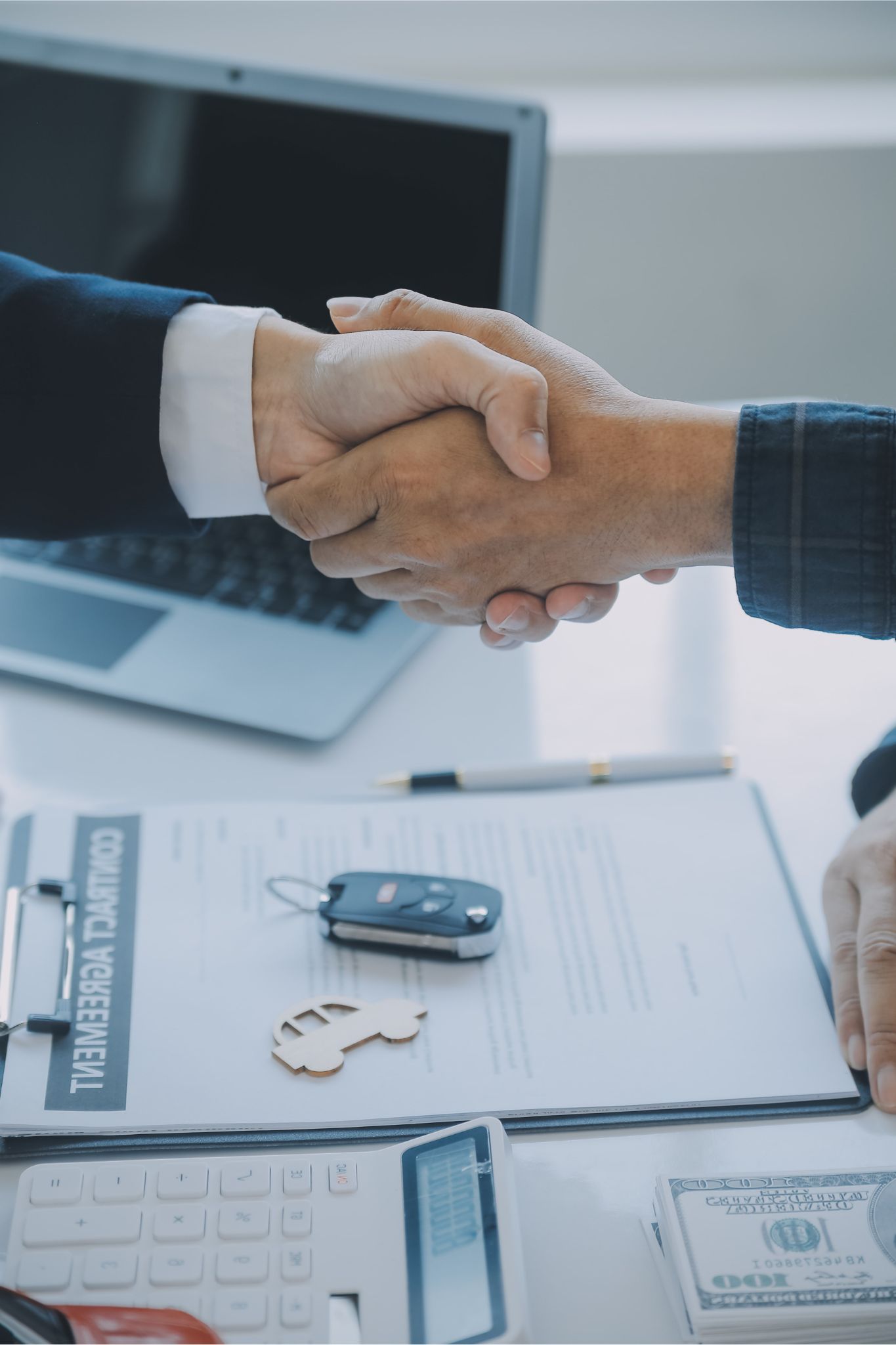 Two people shaking hands over vehicle insurance services solutions contract with keys and documents